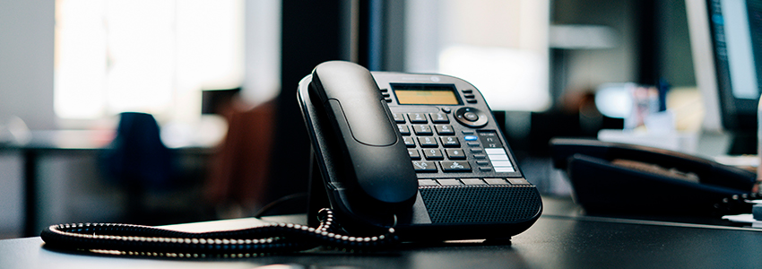 Un telefono fisso nero è appoggiato ad una scrivania d'ufficio